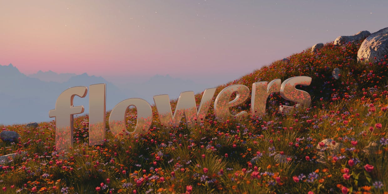 the word "flowers", metallic, sits in a field of flowers on a mountain overlooking the faint haze of mountains in the background at sunset